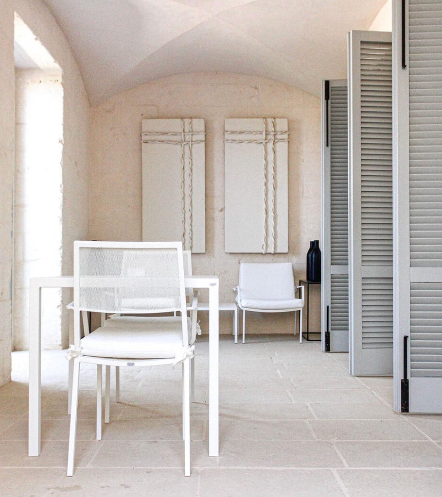 Elegant Mediterranean hotel room with limestone walls, ornate chandelier, white canopy bed, and arched window overlooking Puglia scenery