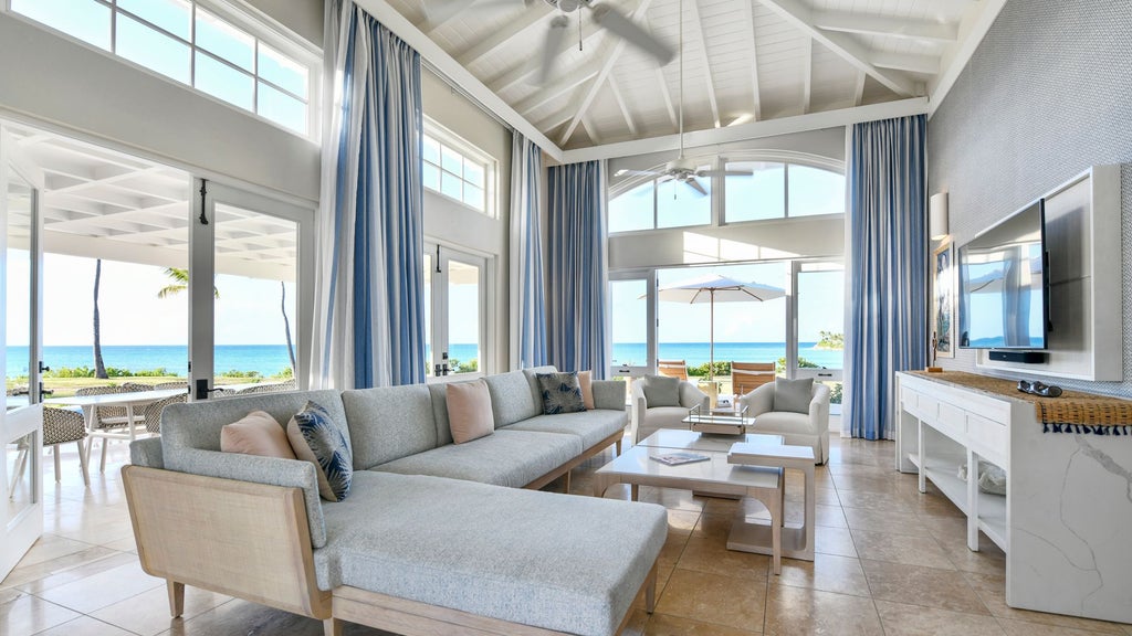 Luxurious Estate Suite with white four-poster bed, elegant coastal decor, and panoramic ocean view through large sliding glass doors in Antigua resort