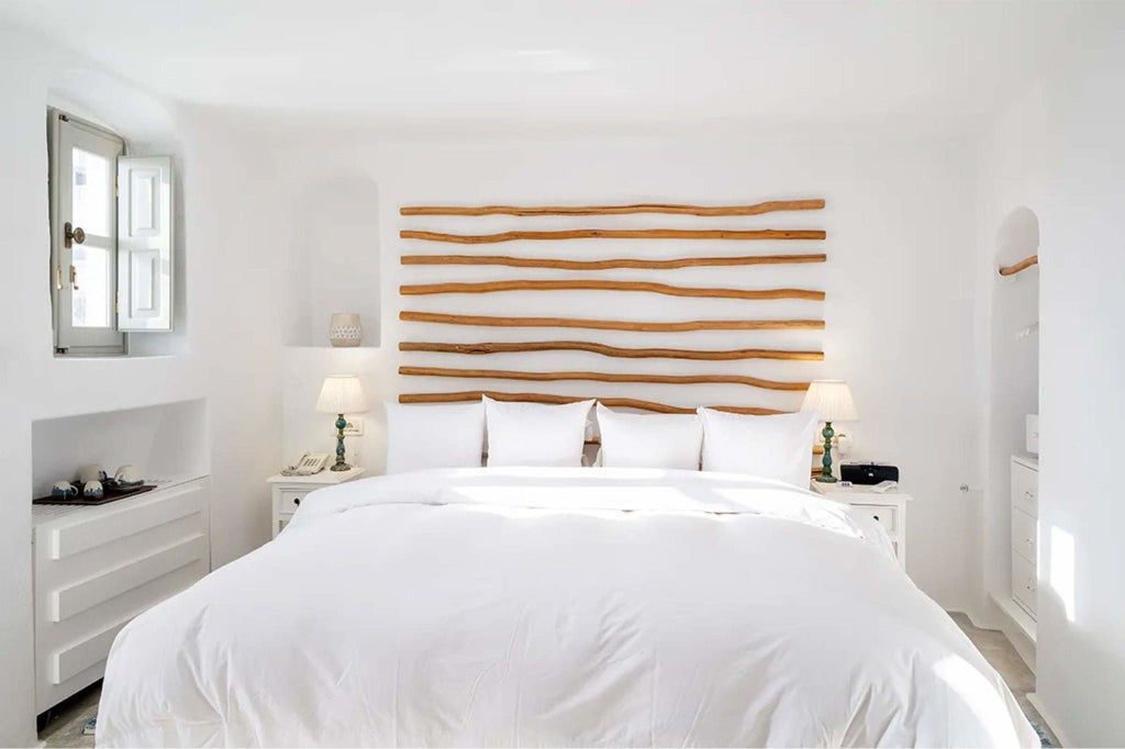 Minimalist white cave-style loft room with arched windows overlooking azure Aegean Sea, featuring sleek modern furnishings and traditional Cycladic architectural design