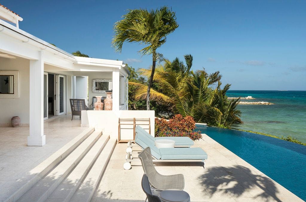 Luxurious beachfront resort with white sand, turquoise waters, lush palm trees, and elegant villas nestled along the pristine coastline of Antigua