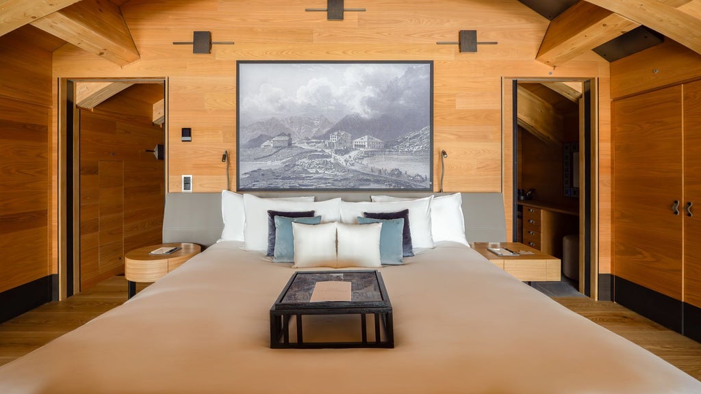 Spacious luxury suite with alpine wood paneling, elegant contemporary furniture, large windows overlooking Swiss mountain landscape at The Chedi Andermatt