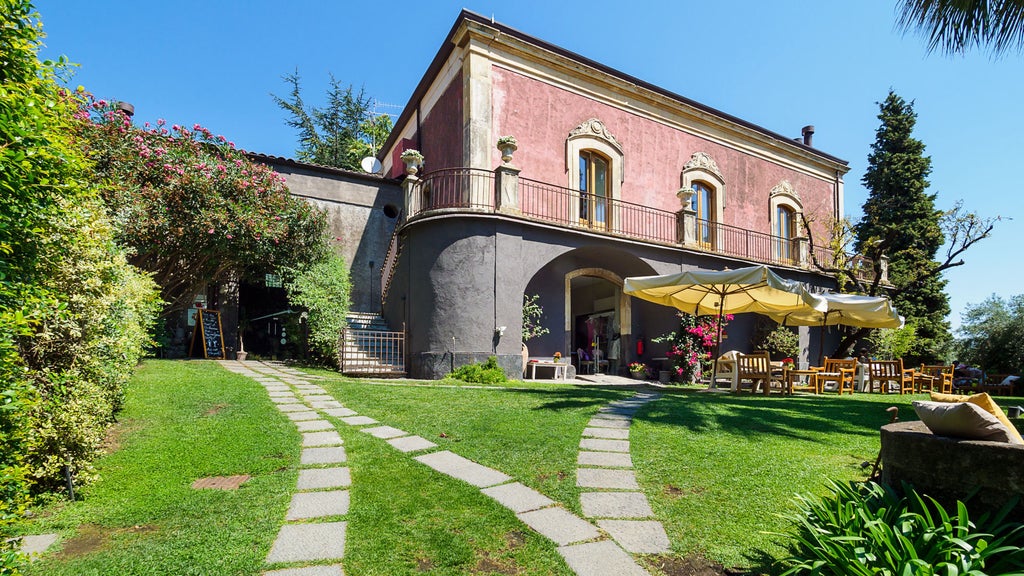 Rustic luxury boutique hotel nestled on Mount Etna's slopes, featuring stone walls, manicured gardens and panoramic vineyard views