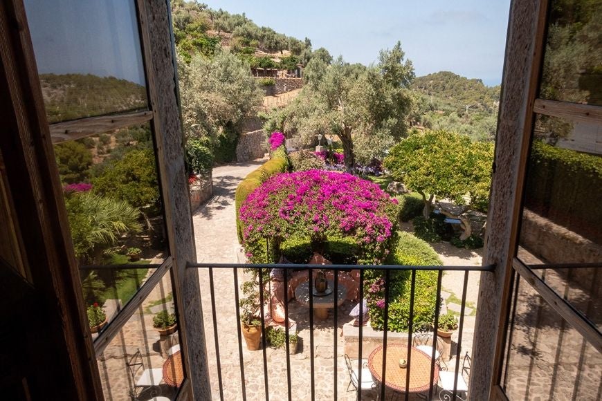 Elegant Spanish luxury suite with white linens, wooden furnishings, stone walls, and expansive windows overlooking scenic landscape at Ca's Xorc Retreat