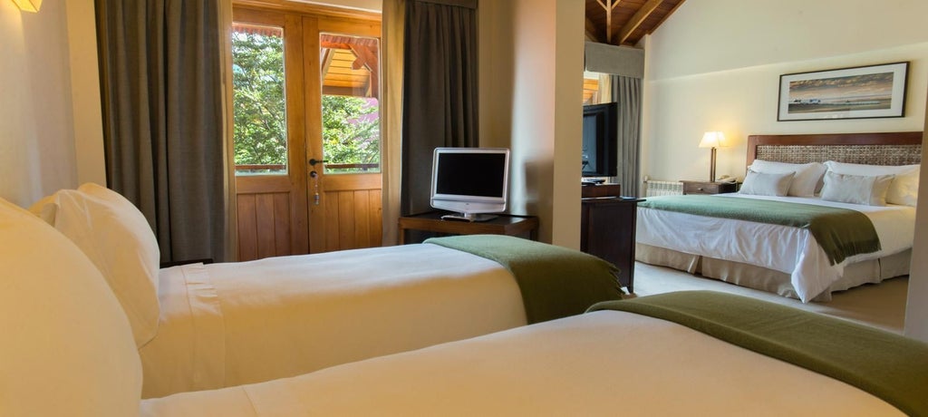 Spacious quadruple standard hotel room with elegant wood furnishings, panoramic mountain views, and cozy alpine-inspired decor at Los Cauquenes Resort in Patagonia, Argentina