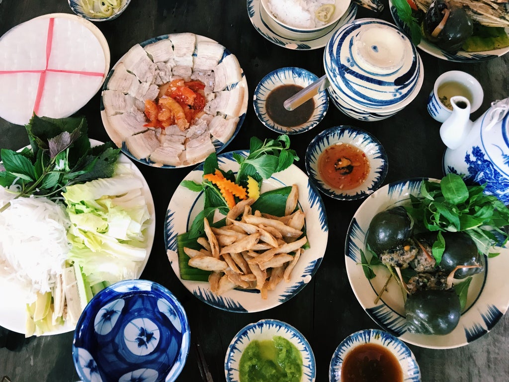 Traditional Thai kitchen with elderly woman teaching cooking, colorful ingredients spread on wooden countertop, warm sunlight illuminating authentic culinary scene