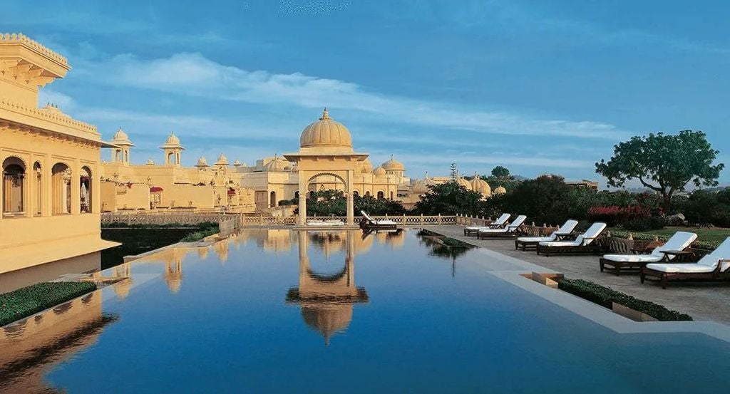 Opulent domed hotel with ornate Rajasthani architecture reflected in serene pool waters, surrounded by manicured gardens at sunset