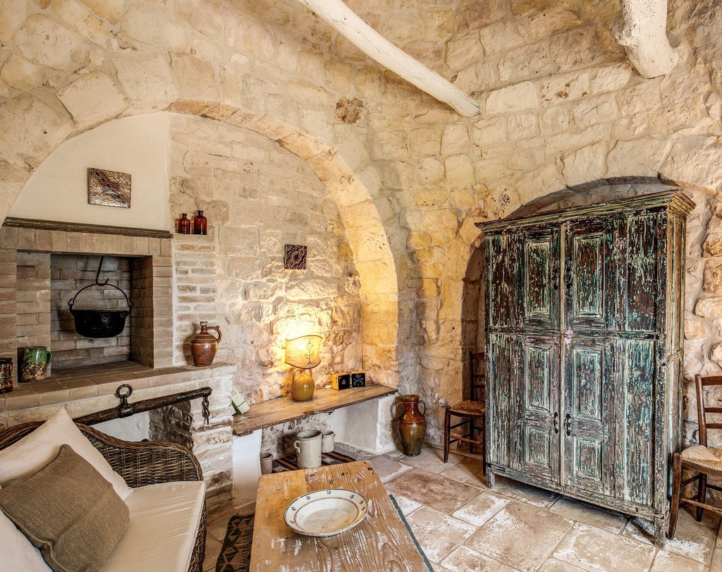 Rustic stone-walled junior suite with elegant Mediterranean decor, plush white bedding, and warm wooden furnishings in scenic Puglia, Italy.