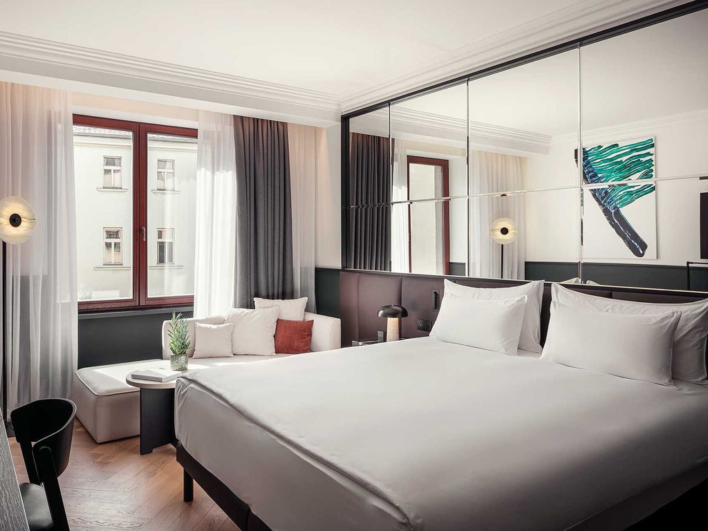 Elegant modern hotel room with plush furnishings, soft neutral color palette, expansive city view through glass doors leading to private balcony in Prague