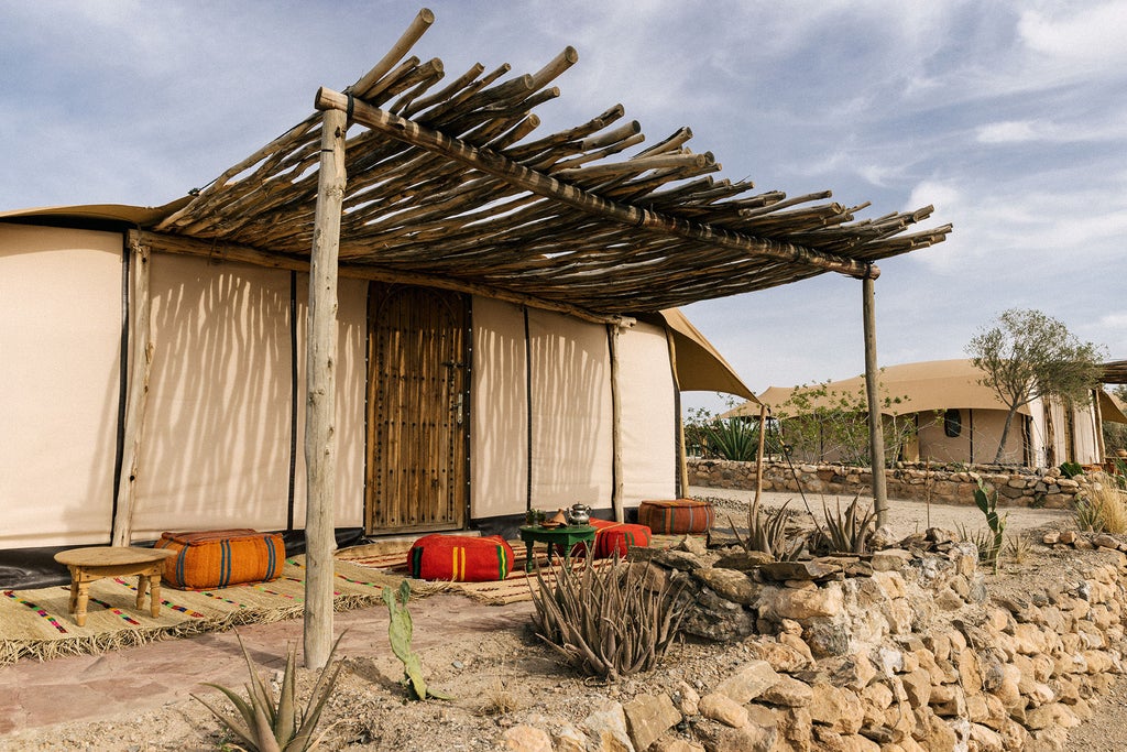 Luxurious desert tent suite with infinity pool overlooking Agafay's sandy dunes, dramatic Atlas Mountains in the golden sunset