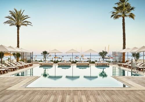 Modern beachfront hotel with infinity pools overlooking Mediterranean Sea, white sun loungers, and elegant palm-lined terraces