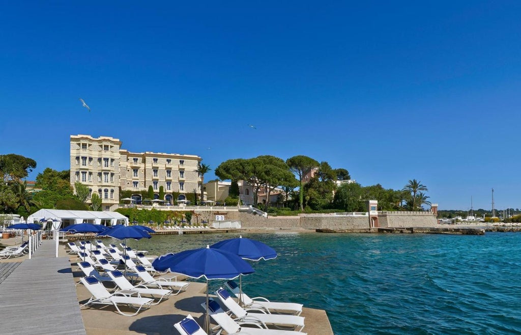 Art Deco seaside luxury hotel with elegant white facade, palm trees, and private beach overlooking the French Riviera's azure waters