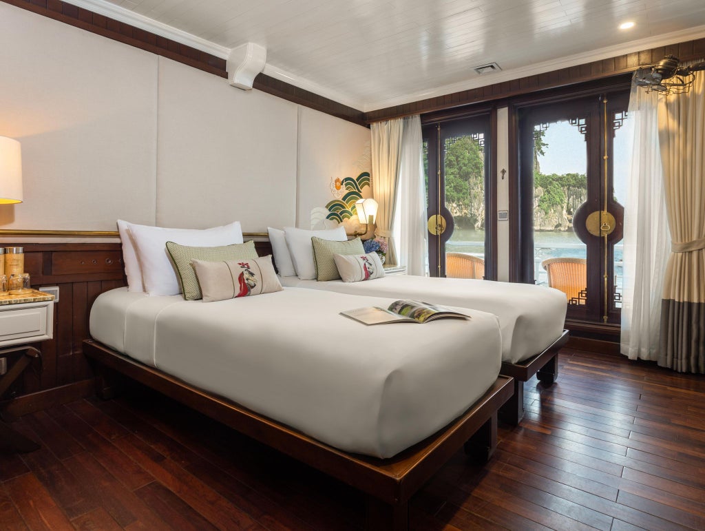 Elegant Deluxe Cabin aboard Bhaya Cruises, featuring rich wooden furnishings, crisp white linens, panoramic windows overlooking tranquil Vietnamese waters