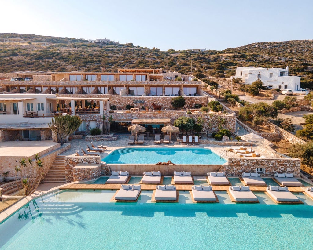 White-washed luxury hotel with infinity pool overlooking Aegean Sea, private balconies, and cascading terraces against blue sky in Greece