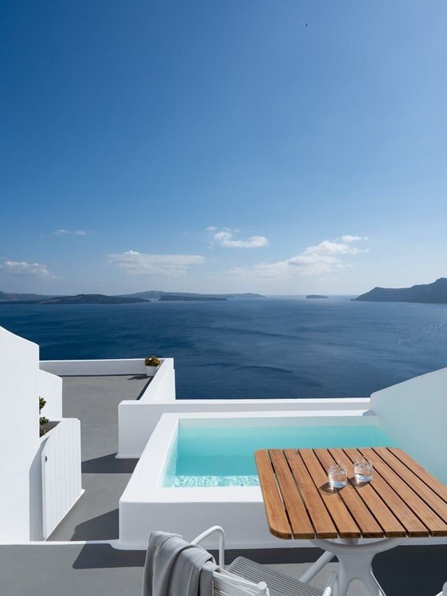 Luxurious white-washed Santorini hotel with curved architecture, infinity pool overlooking azure Aegean Sea and dramatic cliffside landscape of Oia