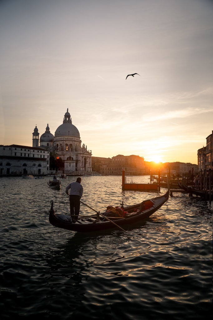 Iconic Venetian canal at sunset, with elegant gondolas gliding past historic pastel-colored palazzos and ornate bridges reflecting in serene waters