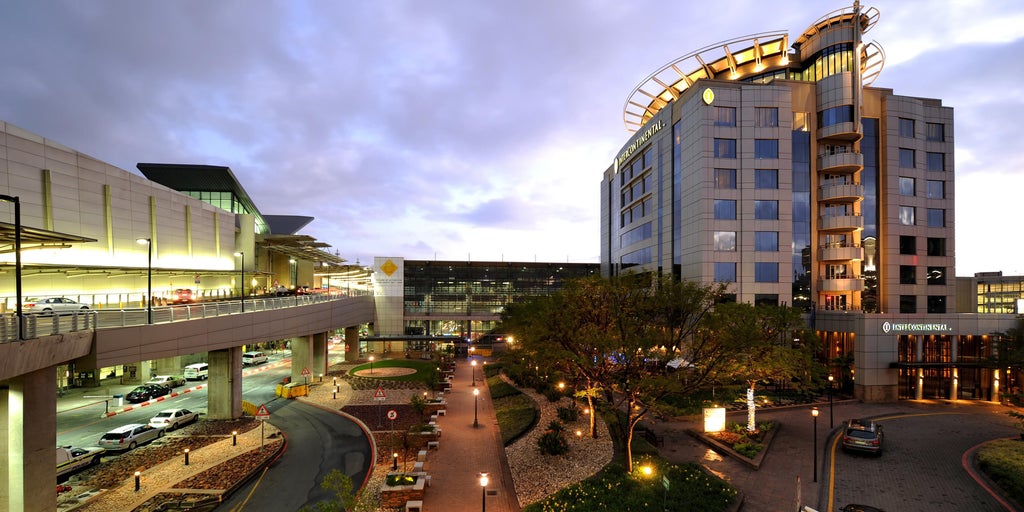 Modern luxury airport hotel with sleek glass facade, marble entrance, palm trees and covered drop-off area in Johannesburg, South Africa