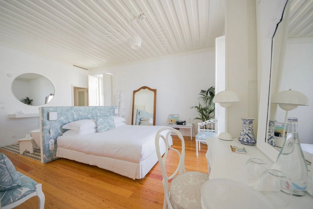 Bright minimalist suite with custom wood furniture, crisp white linens, exposed beam ceiling, and natural light through arched window