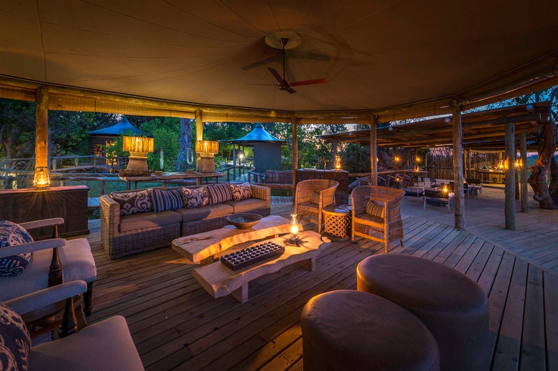 Elevated luxury safari tent with private deck overlooking Okavango Delta wetlands, surrounded by lush papyrus at sunset