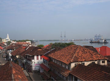 Colonial-style luxury waterfront hotel with red-tiled roofs, white facade, traditional arched windows and wooden balconies overlooking Kochi harbor