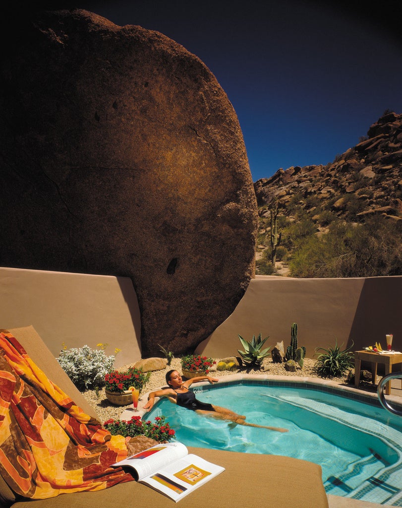 Desert luxury resort with adobe-style buildings nestled against rugged mountains, featuring a pristine pool and elegant outdoor lounging areas