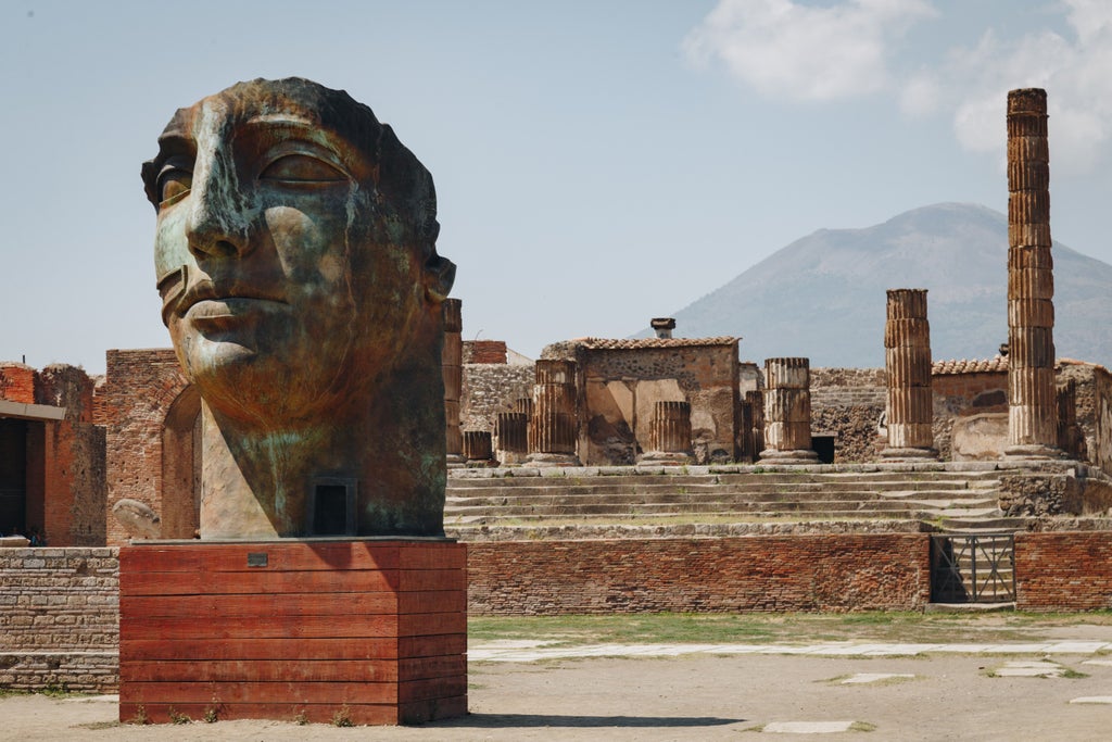 Ancient Roman ruins of Pompeii with well-preserved stone streets, columns and Mount Vesuvius volcano looming in the background at sunset