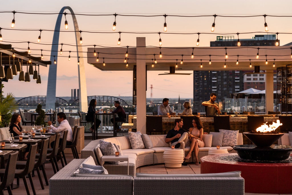 Sleek glass high-rise hotel with dramatic arch design illuminated at dusk, reflecting city lights against the St. Louis skyline