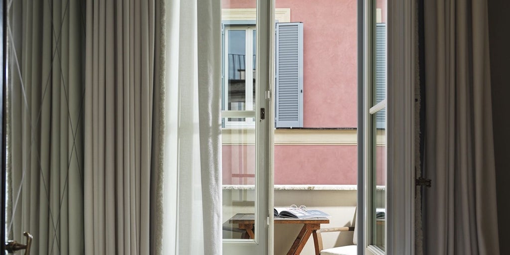 Elegant neutral-toned luxury hotel room with plush white bed, refined Italian marble bathroom, and soft ambient lighting in Roma.