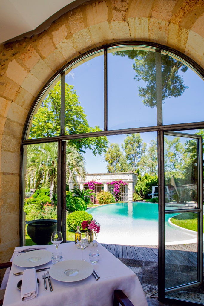 Historic French château hotel with elegant limestone facade, surrounded by manicured gardens and century-old pine trees at sunset