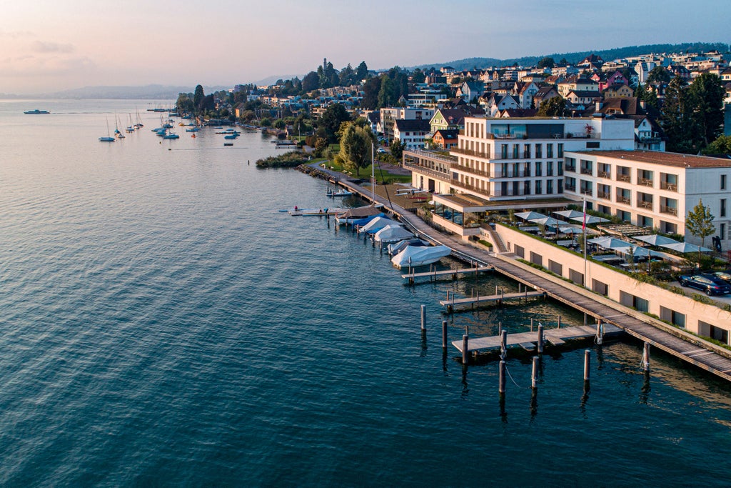 Modern lakeside hotel with floor-to-ceiling glass windows reflecting Lake Zurich, private balconies, and contemporary white architecture