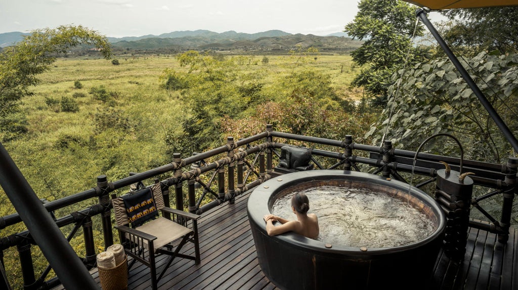 Luxurious safari-style tent room with canopy bed, hardwood floors, rustic furnishings and panoramic views of Thai jungle landscape