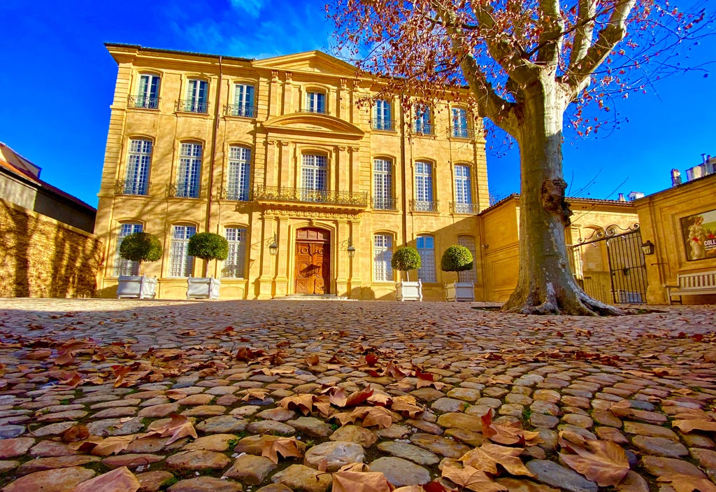 Elegant painters working en plein air in lavender-lined Provençal street, capturing sunlit facades of historic limestone buildings in warm afternoon light