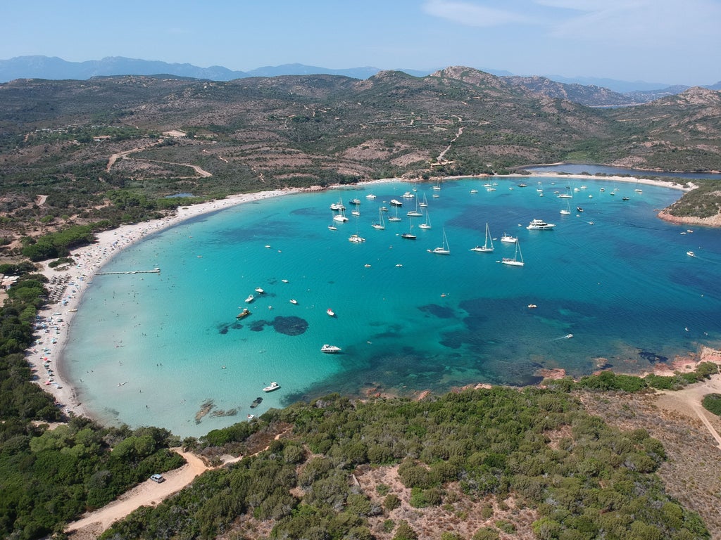 Aerial view of Porto-Vecchio, Corsica showing turquoise Mediterranean bay, luxury yachts, historic citadel and rolling mountains