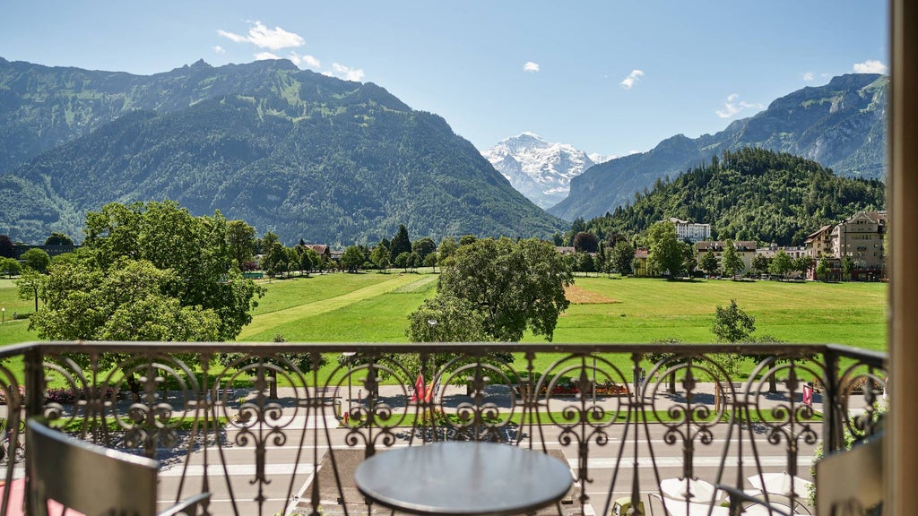 Grand hotel exterior with Belle Époque architecture, snow-capped Alps backdrop, manicured gardens and ornate balconies in Interlaken