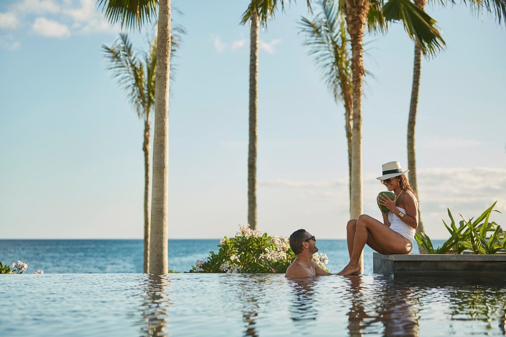 Luxurious beachfront resort with infinity pools cascading to private lagoon, surrounded by palm trees and oceanfront cabanas at sunset