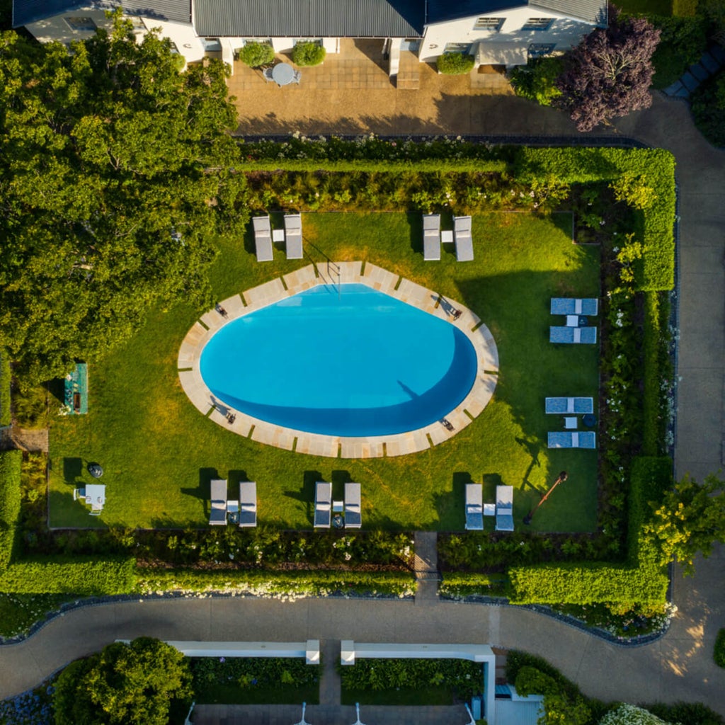 Elegant white Cape Dutch style luxury hotel facade with green shutters and manicured gardens in Franschhoek wine valley at sunset