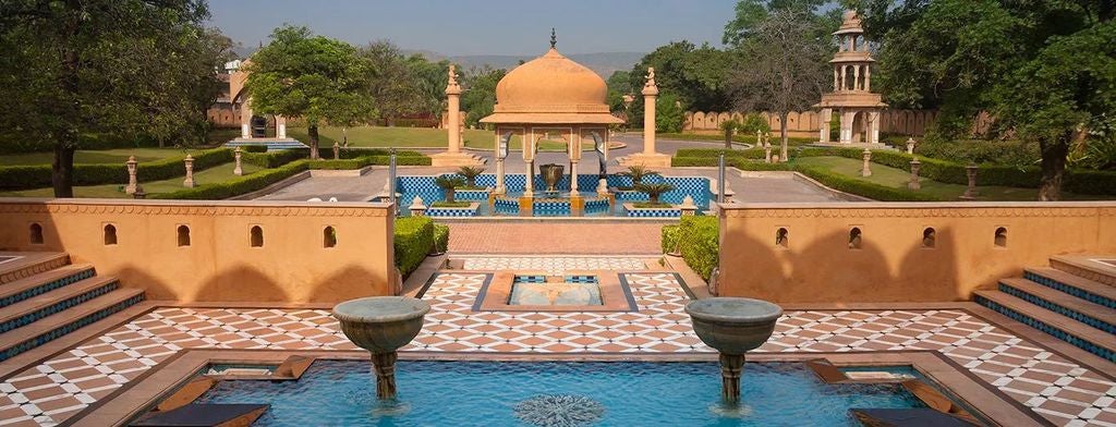 Opulent Indian palace hotel with ornate domes and archways surrounded by manicured gardens and reflection pools at sunset