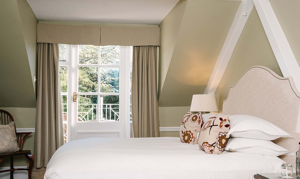 Luxurious Coach House Suite at Chewton Glen Spa, featuring elegant wood furnishings, plush bedding, and large windows overlooking lush countryside