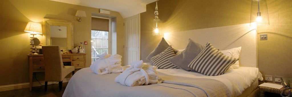 Elegant boutique hotel bedroom with plush white bedding, soft neutral tones, minimalist decor, and expansive window revealing scenic countryside landscape