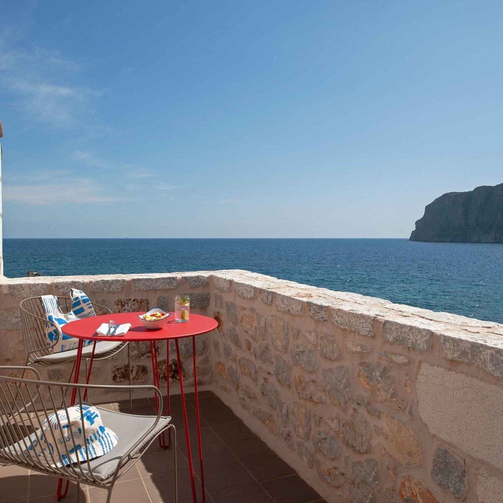 Elegant stone-walled loft suite with wooden beam ceiling, plush white bed, and Mediterranean Sea view at luxurious seaside Greek hotel