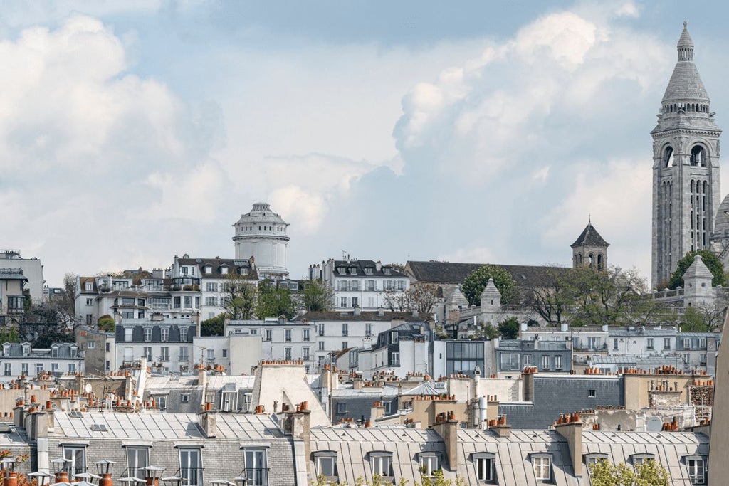 Elegant Parisian boutique hotel with art deco facade, soft pink exterior, ornate balconies, and chic street-level entrance in trendy South Pigalle neighborhood