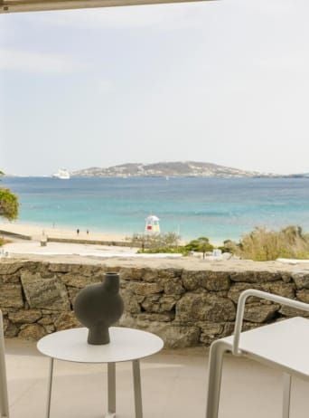 Luxurious whitewashed hotel terrace overlooking azure Aegean Sea, with elegant minimalist design, infinity pool, and Mykonos landscape beyond