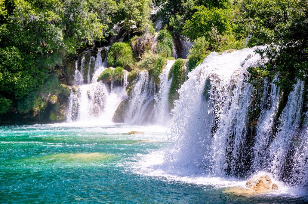 Scenic wooden boardwalk winding through lush forest leading to majestic Skradinski Buk waterfall cascading into turquoise pools at Krka