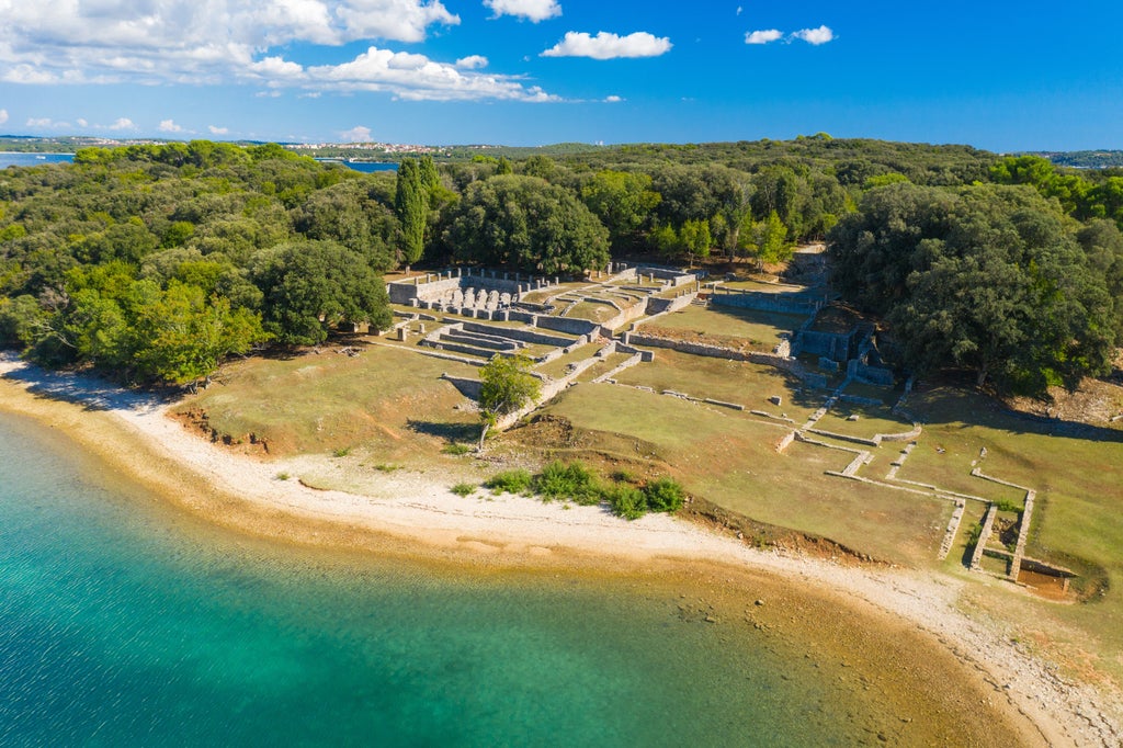 Professional cyclists explore pristine trails on luxurious Brijuni Island, with turquoise Adriatic waters and ancient Roman ruins in background