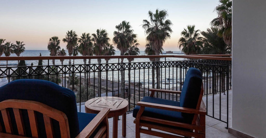 Spacious two-bedroom suite with modern design, plush white bedding, sleek furnishings, and panoramic view of Cyprus coastline at luxurious seaside resort