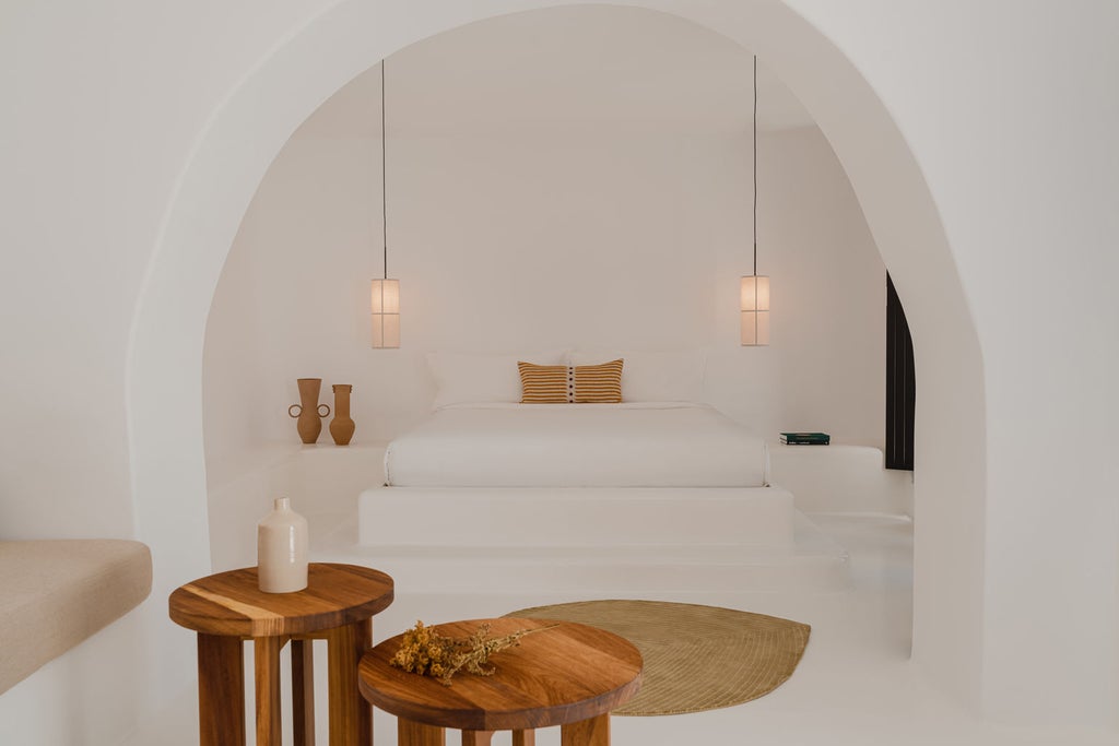 Modern minimalist suite with private plunge pool overlooking Santorini's caldera, featuring white walls and natural wood furnishings