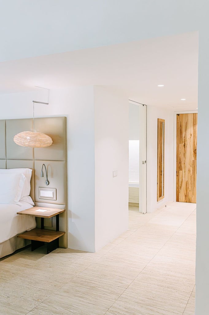 Elegant whitewashed Menorcan-style superior hotel room with minimalist design, crisp linens, and warm natural light streaming through rustic window