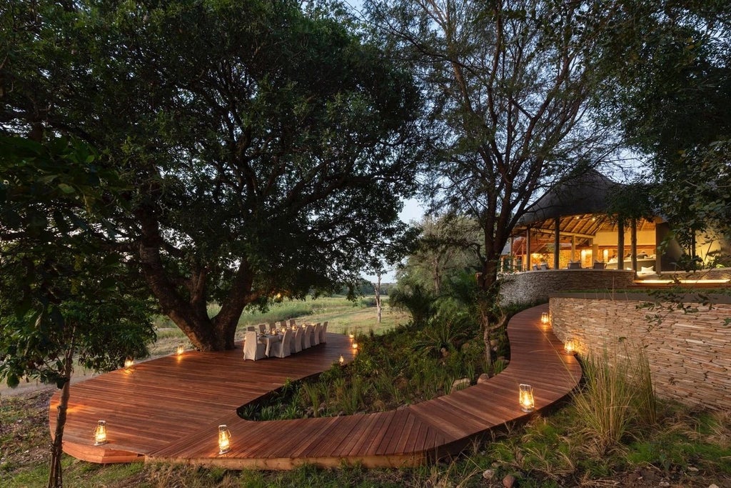 Elegant safari lodge with thatched roof overlooking Sabi Sand riverbank, surrounded by lush African bushveld and private deck seating