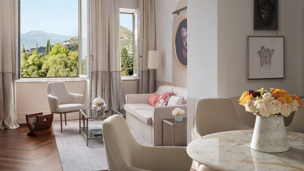 White luxury hotel with arched windows and columns spanning a cliffside terrace overlooking the Mediterranean Sea and Mount Etna