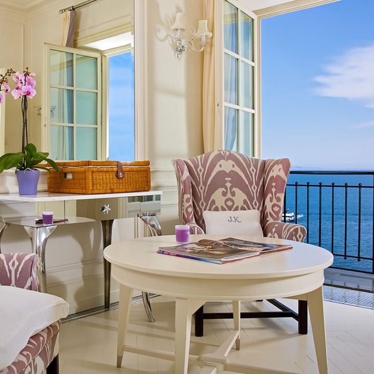 Elegant white Mediterranean hotel overlooking Capri's blue waters, featuring classic columns, manicured gardens, and panoramic terrace views