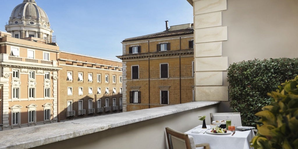 Elegant balcony suite at J.K. Place Roma with plush white bedding, marble accents, and sweeping views of Italian architectural cityscape